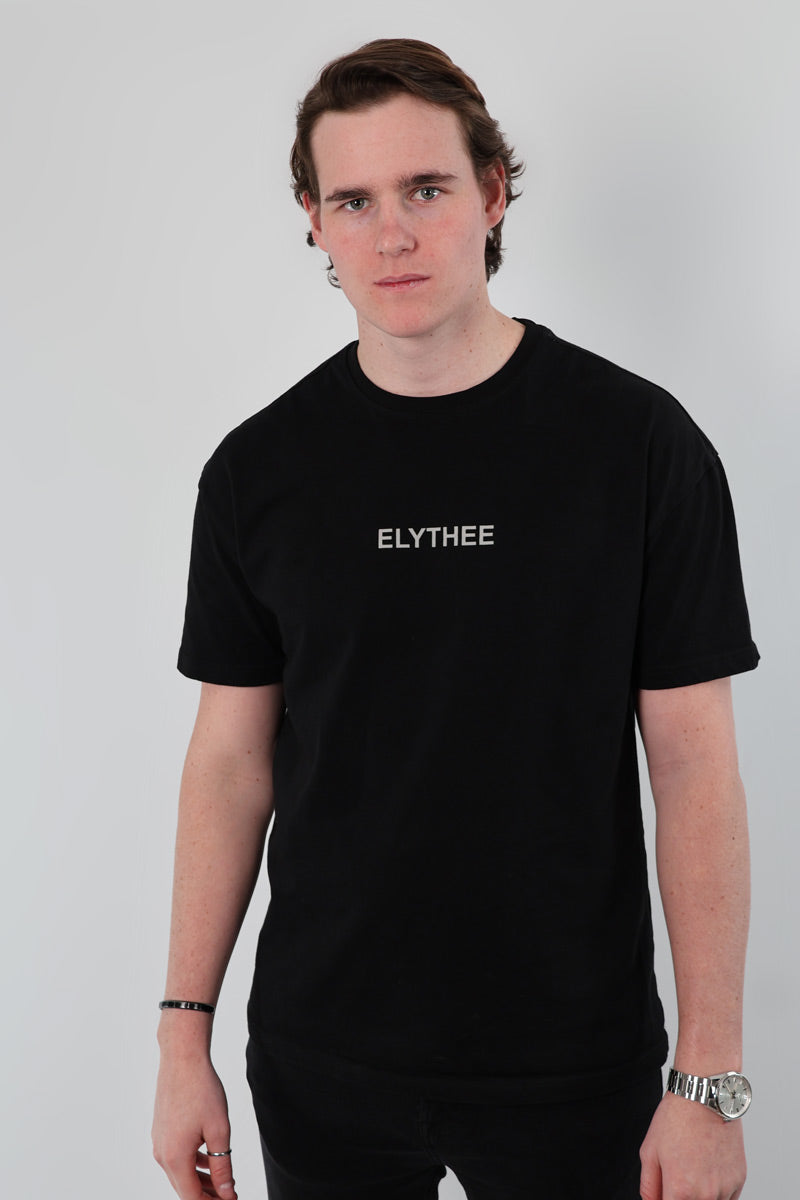 A person wearing a black Mythical Whisper Oversized T-Shirt stands against a plain background, looking at the camera.