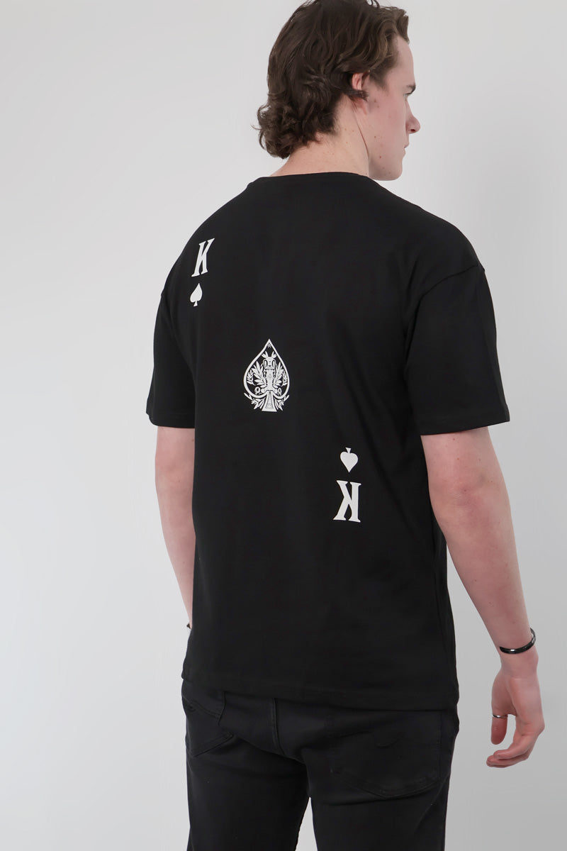 Person wearing an Olympian Royale Oversized T-Shirt featuring playing card symbols, including a spade and the letter K, on the back.