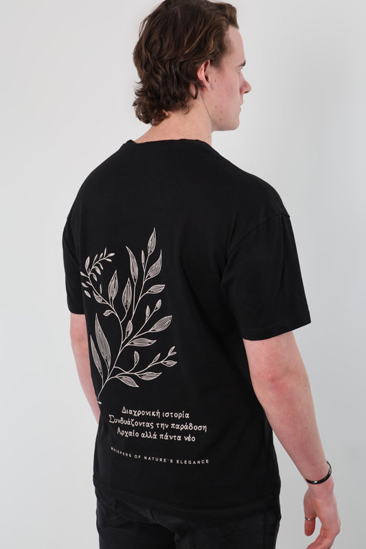 A person, facing away from the camera, is wearing the Mythical Whisper Oversized T-Shirt with a plant design and Greek text on the back.