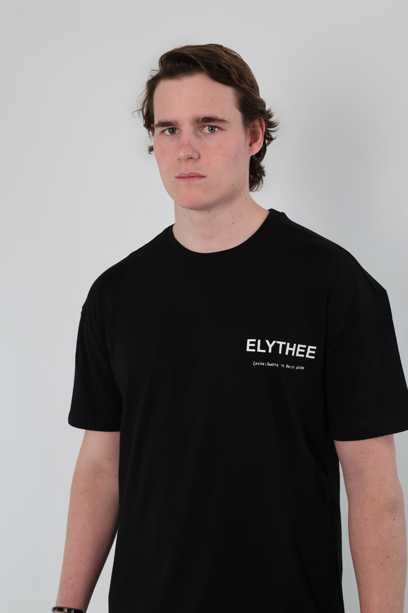 A brown-haired person wearing a black Olympian Royale Oversized T-Shirt stands in front of a plain light background.