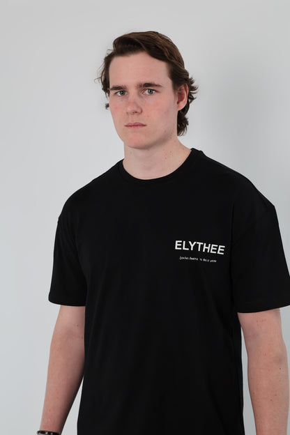 A brown-haired person wearing a black Olympian Royale Oversized T-Shirt stands in front of a plain light background.