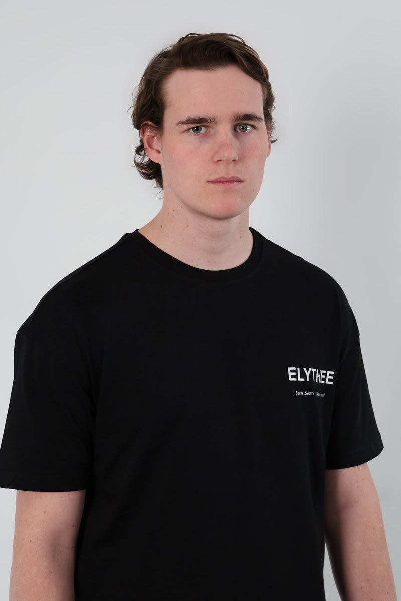 A person wearing an Olympian Royale Oversized T-Shirt with ELYTHEE text on the front stands against a plain white background.
