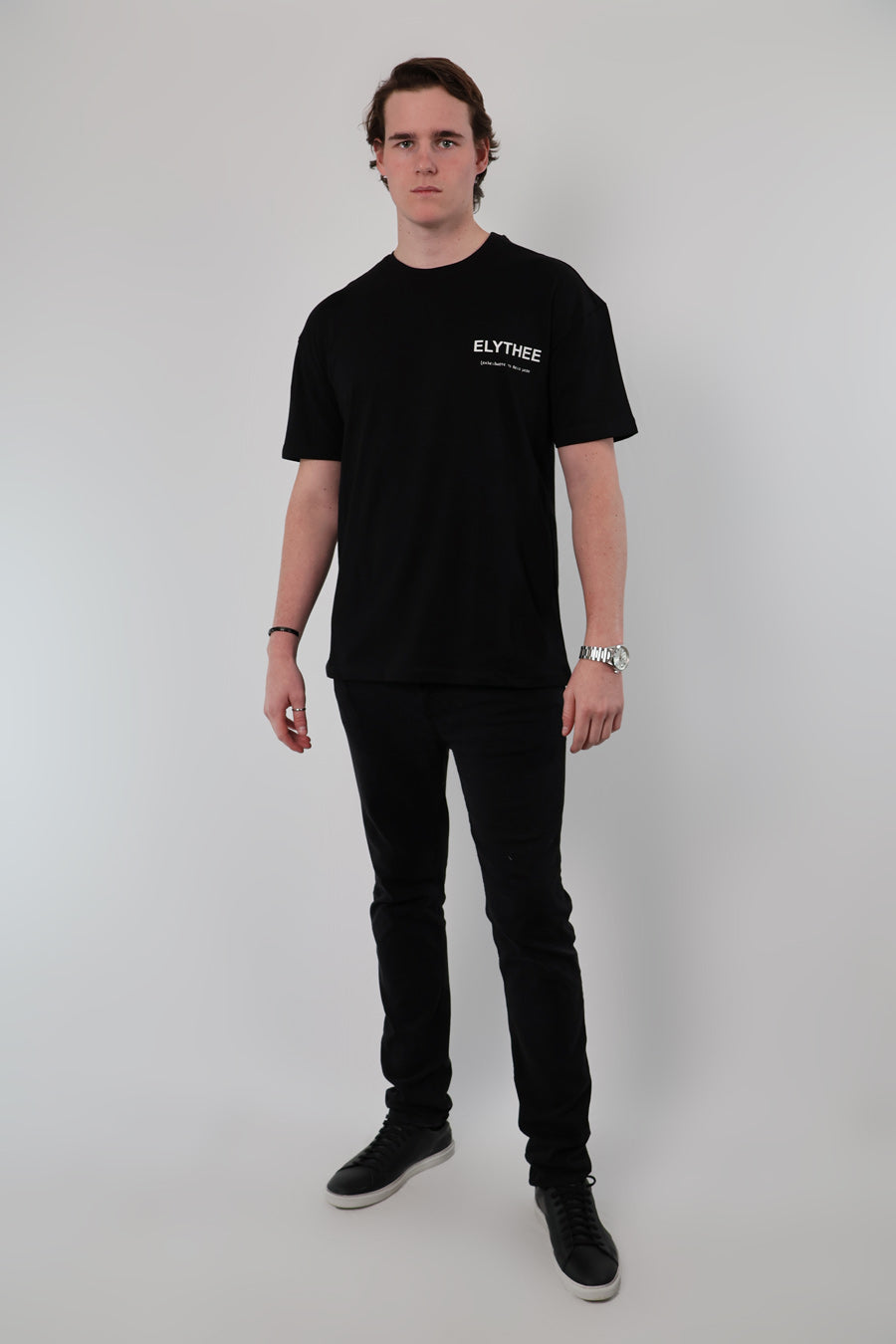 A person wearing a black Olympian Royale Oversized T-Shirt and dark pants stands against a plain light background.