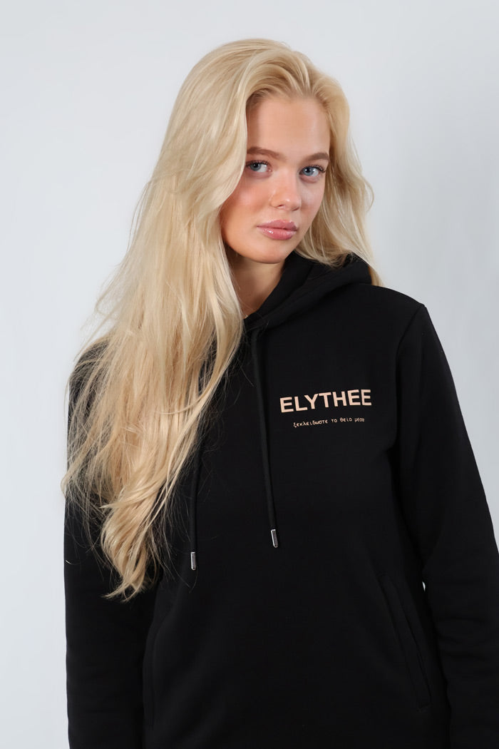 A person with long blond hair wears a Legacy Hoodie - Unisex, made from premium cotton, standing against a plain white background.