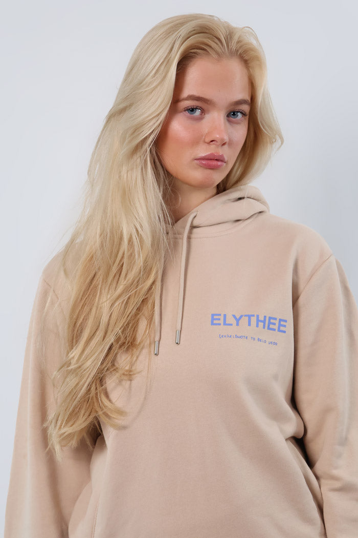 A person with long blond hair wearing the Mythos Essence Hoodie in beige featuring ELYTHEE text.