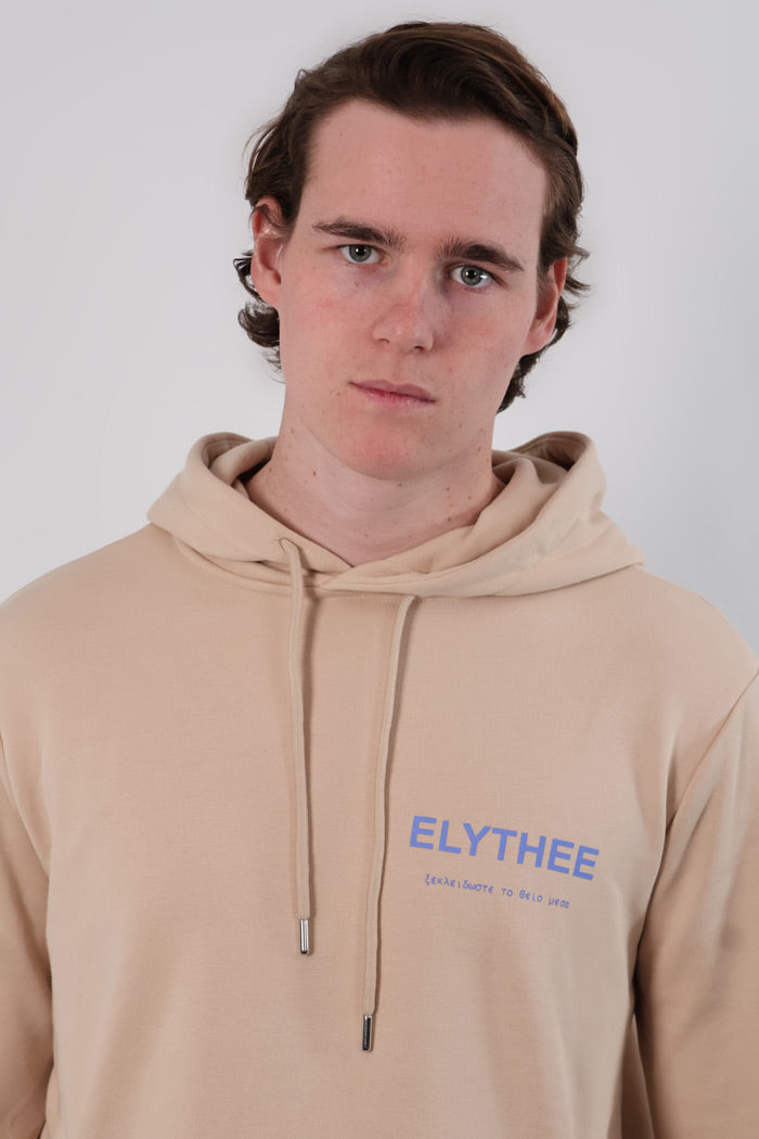A person wearing the Mythos Essence Hoodie, featuring ELYTHEE text, stands against a plain background.