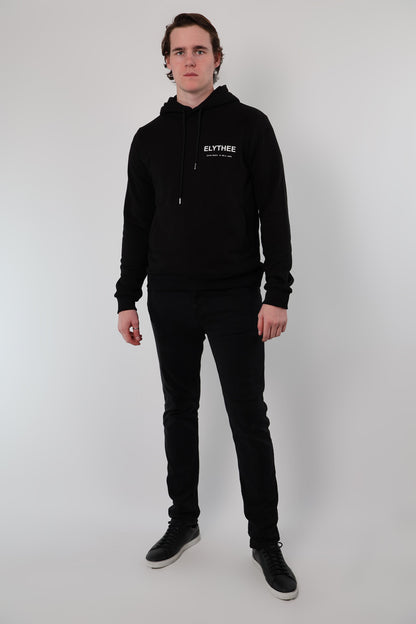 A person stands against a plain background wearing the Mythos Essence Hoodie, black pants, and black sneakers.