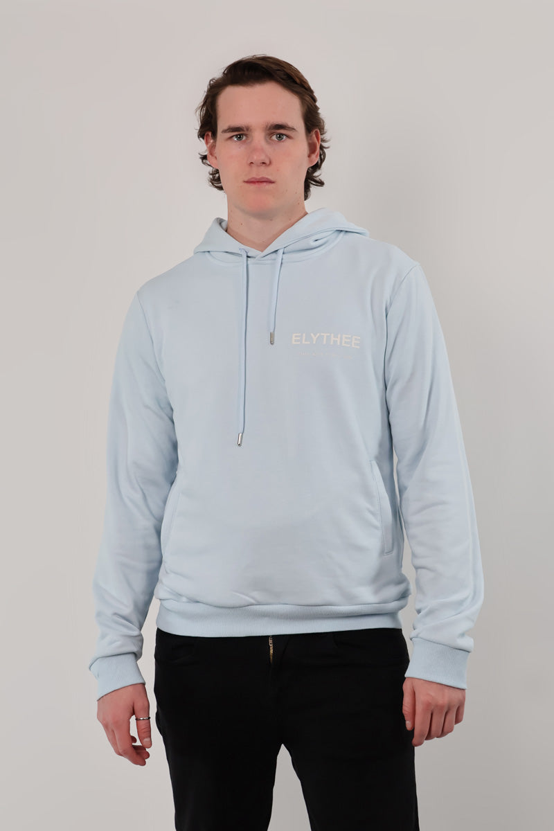 Someone wearing the Mythos Essence Hoodie in light blue, standing against a plain background.