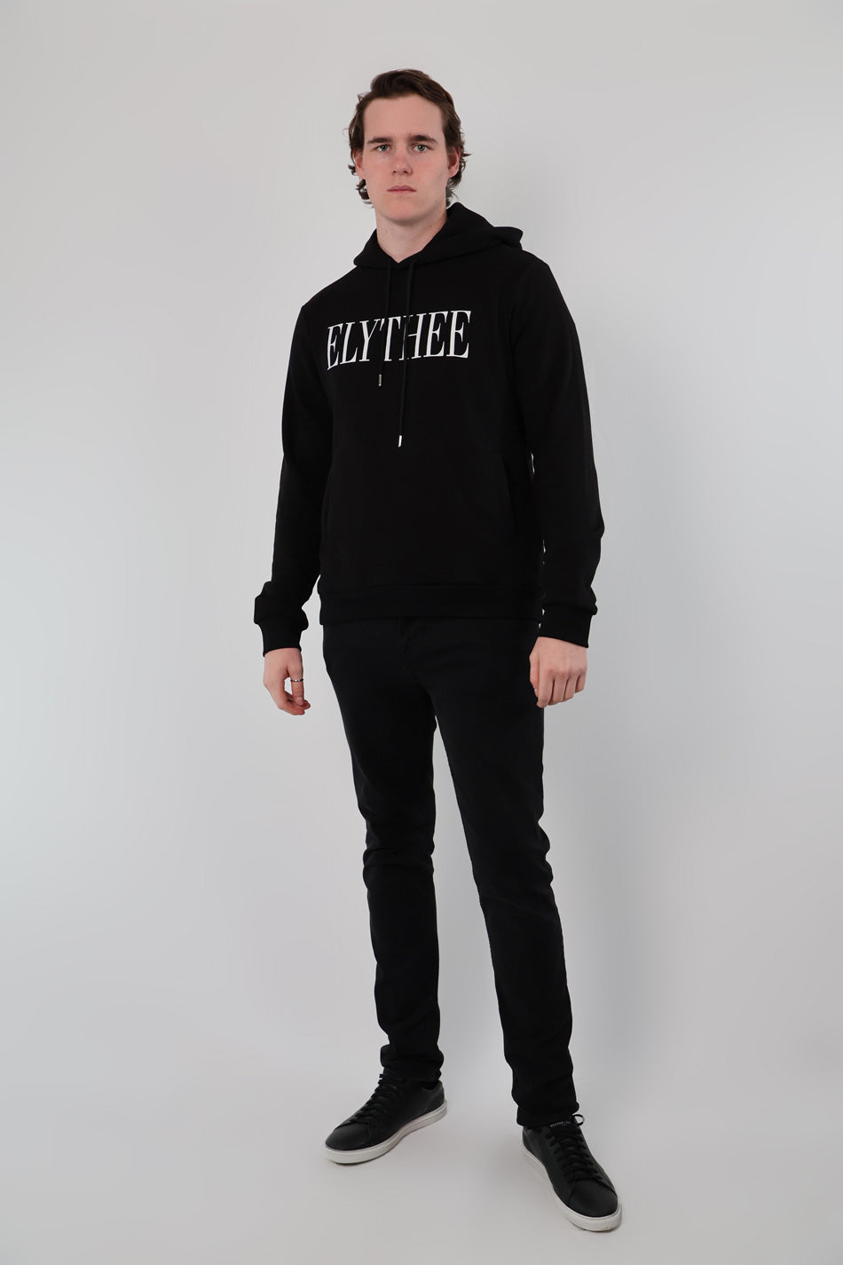 Against a plain white background, a person wears a sleek black unisex Nectar Nomad Hoodie, paired with matching pants.