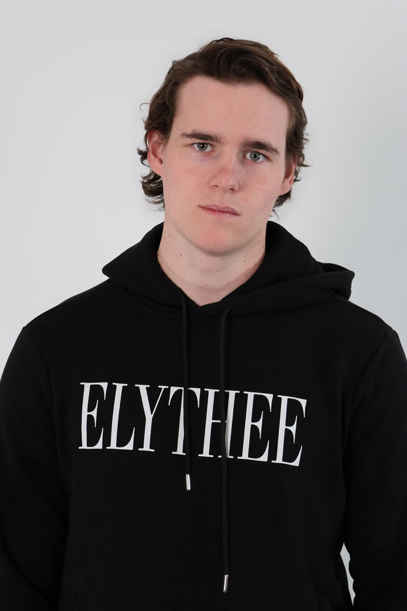 A person stands against a plain white background wearing a stylish and comfortable black Nectar Nomad Hoodie with ELYTHEE emblazoned on it, ideal for modern explorers.