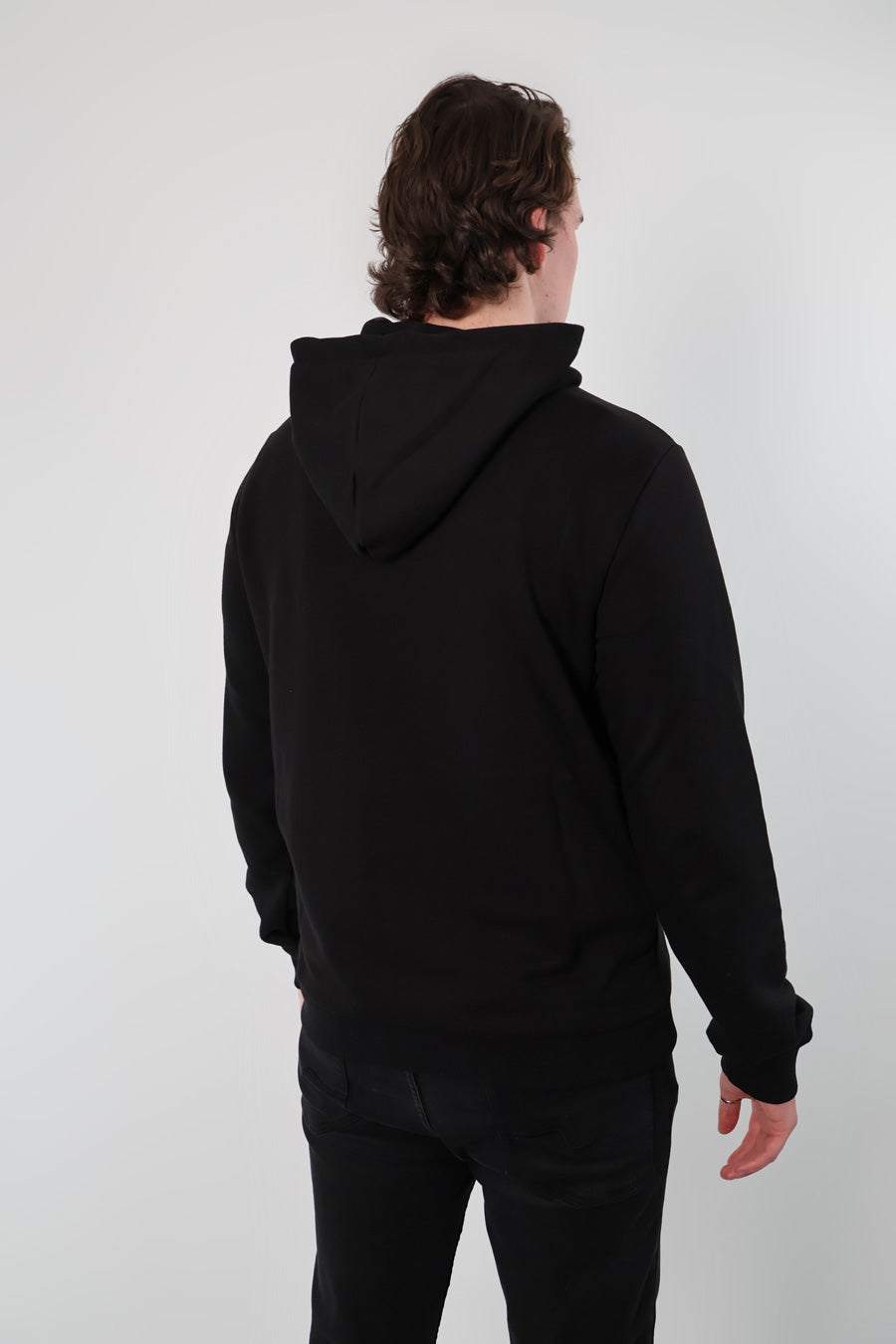A person wearing a Nectar Nomad Hoodie and black pants stands with their back to the camera, blending seamlessly into the plain background.