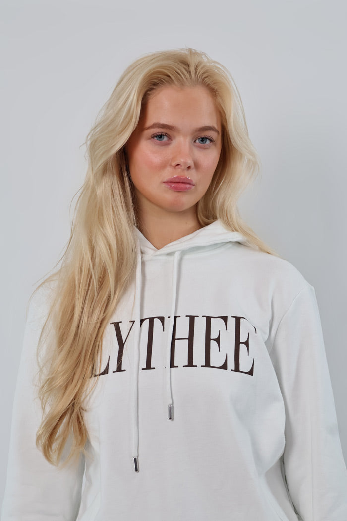 A person with long blonde hair wears a white Nectar Nomad Hoodie with LYTHEE printed on it, standing against a plain background.